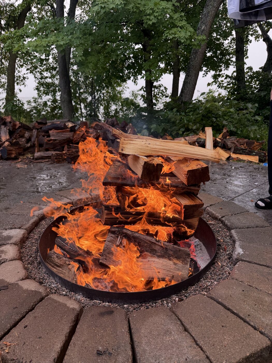 Fire burning in a stone ring on the shore, split oak stacked behind