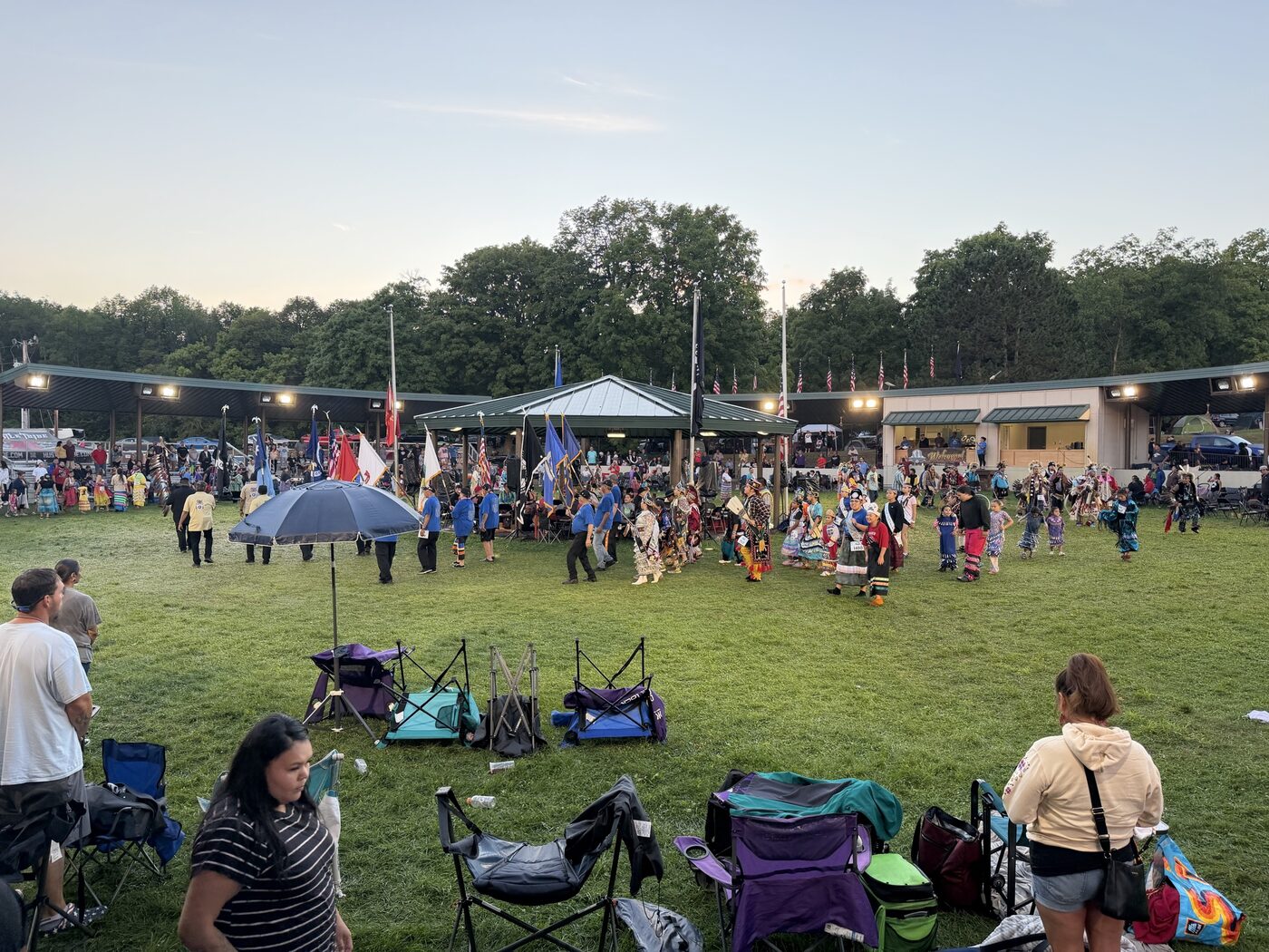 Grand entry at the powwow grounds, flags carried in under the arbor